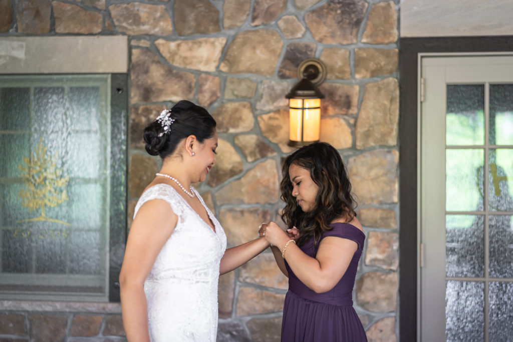 Beatrice is getting ready for her wedding with her friend helping her put on a bracelet inside one of the rooms at Mohawk House Sparta, NJ.