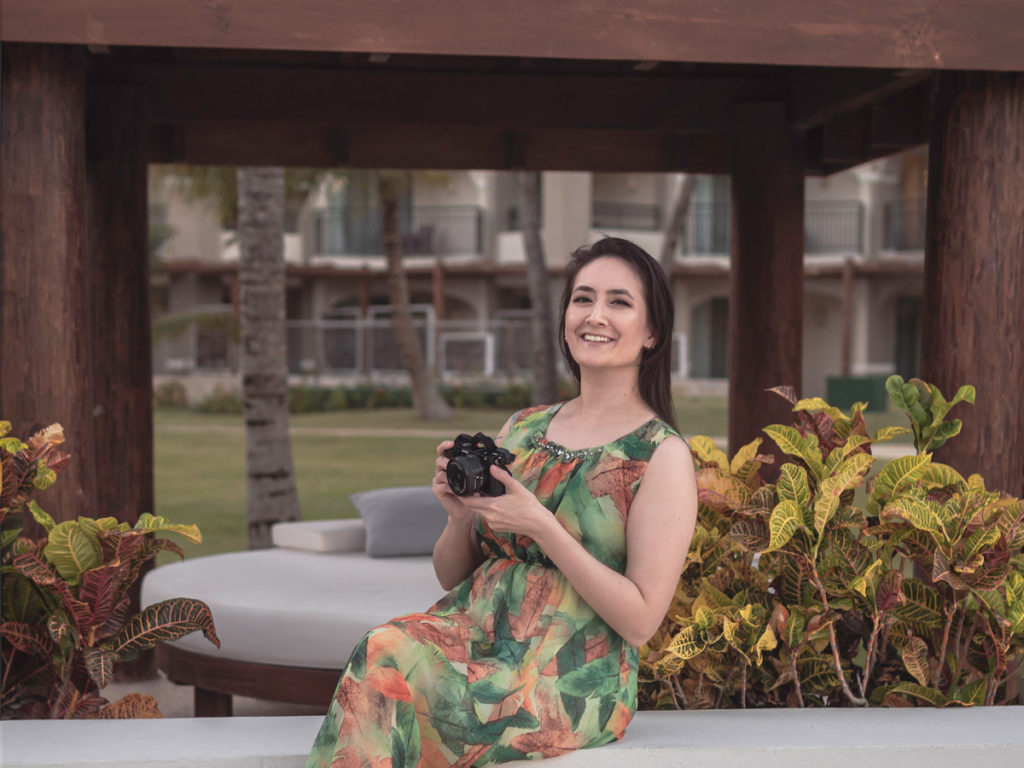 Portrait of me smiling for the camera while holding a black Sony a6400 and wearing a green dress in anticipation to quit my corporate job. 