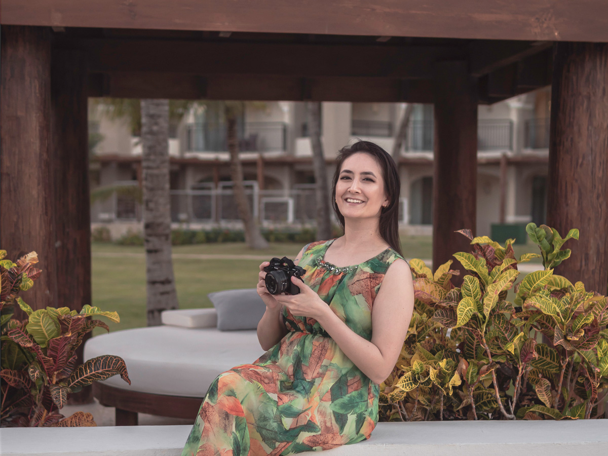 Portrait of Erin Donahue smiling for the camera while holding a black Sony a6400 and wearing a green dress.