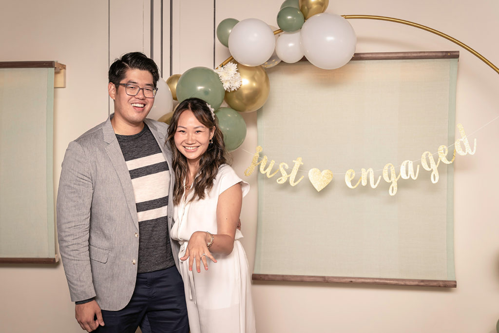 Tom and Janet standing in front of the "just engaged" sign in a private room at Rule of Thirds, Brooklyn.