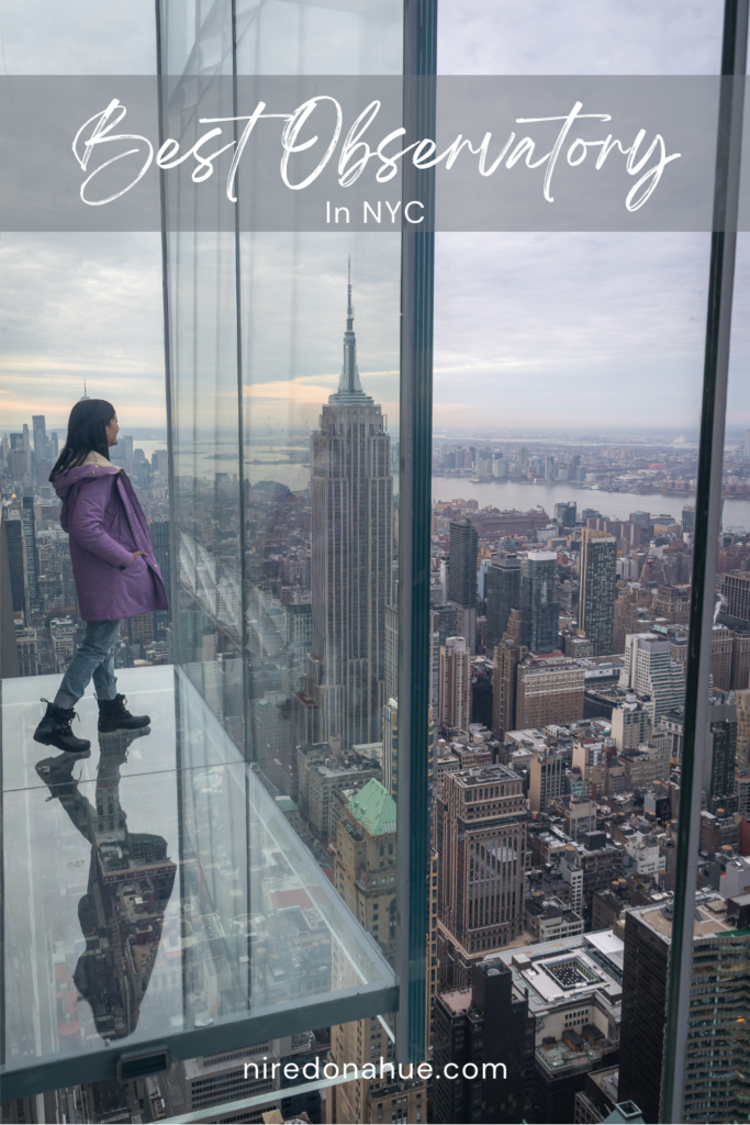 Pinterest Pin standing in a glass box overlooking the city, the Empire State Building can be seen from Summit One, one of the best observatories in NYC.