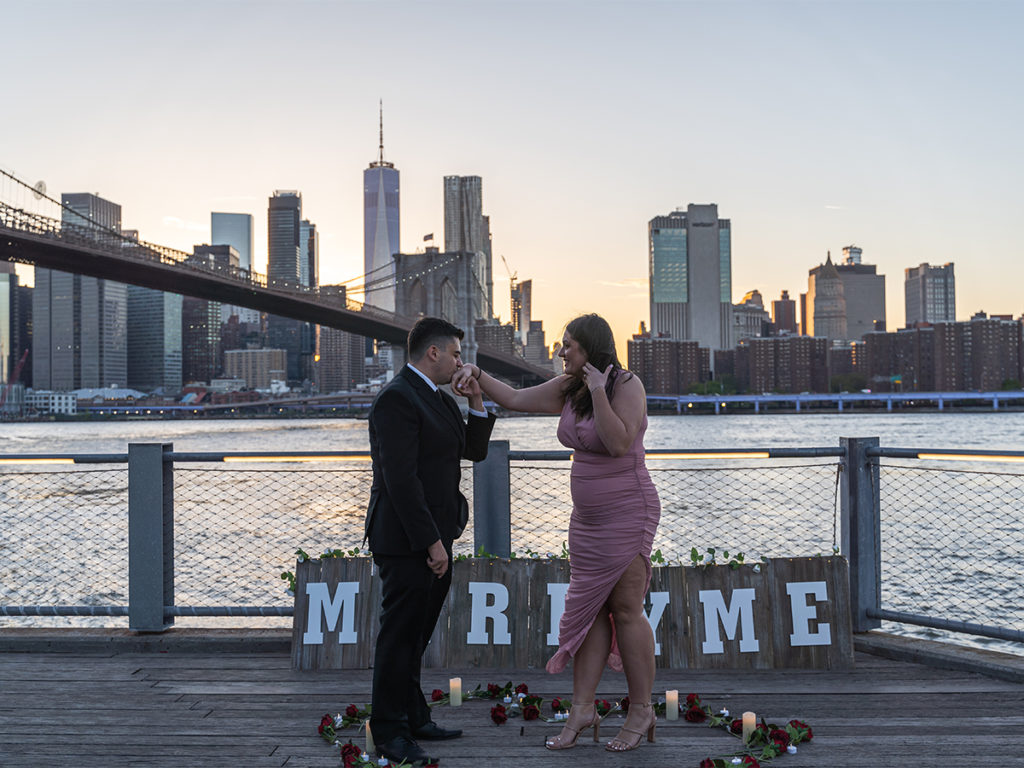 Jane's Carousel Brooklyn proposal with a "marry me" sign in the background.