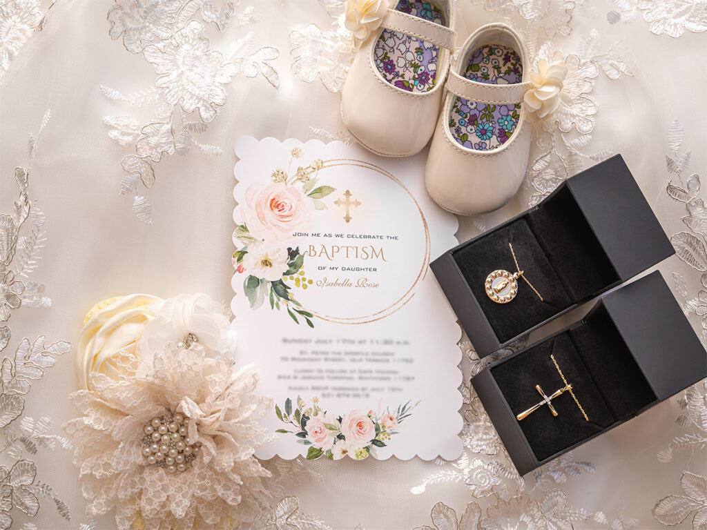 Invitation of a baby's baptism adorned with the baby's shoes and necklace in Long Island.