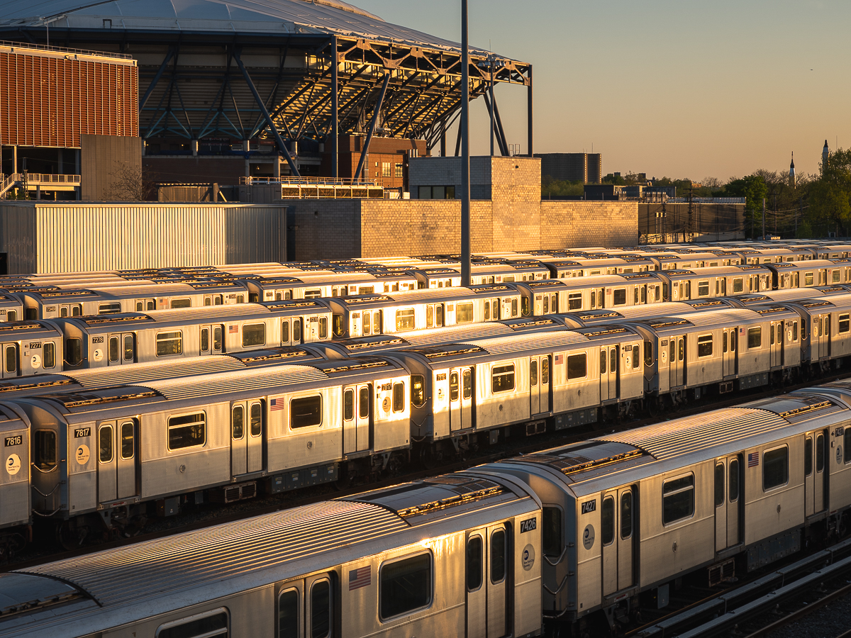 Rows of MTA subway trains in front of Arthur Ashe Stadium reflect the golden hour sun.