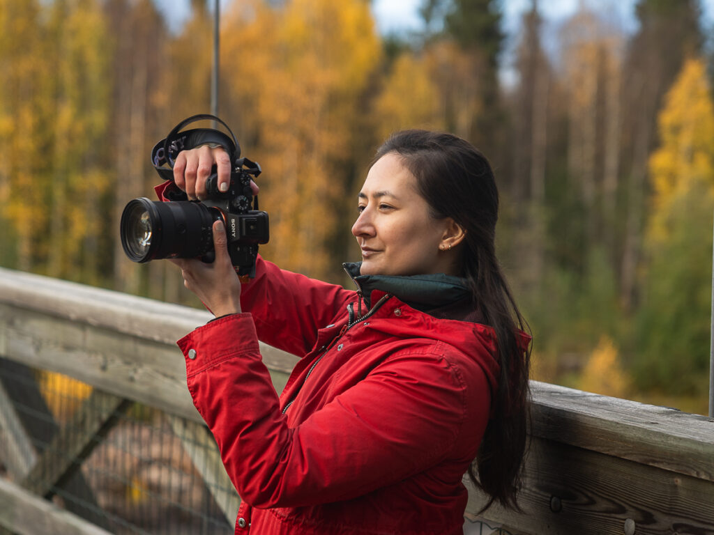 Holding up a camera with fall foliage in the background.