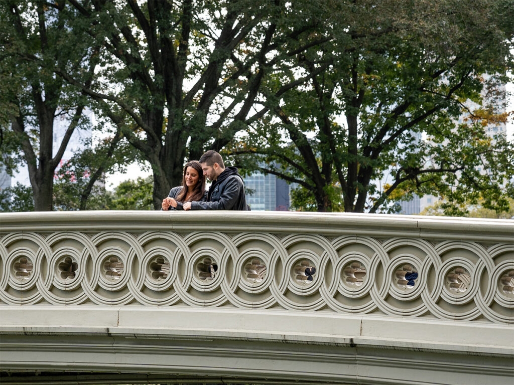 The newly engaged couple admire the engagement ring on the Bow Bridge.