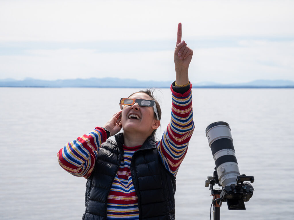 Looking up and pointing at the sky with solar eclipse glasses and a camera to photograph the total solar eclipse.