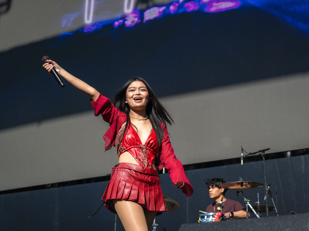 Lyn Lapid, wearing red, smiles and reaches her microphone out to the crowd at Head In The Clouds Festival.