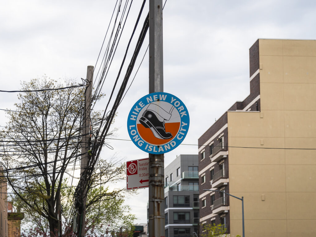 The Hike New York Long Island City path is marked by a series of street signs with a logo of a cuffed trouser leg and black dress shoe in midstride.