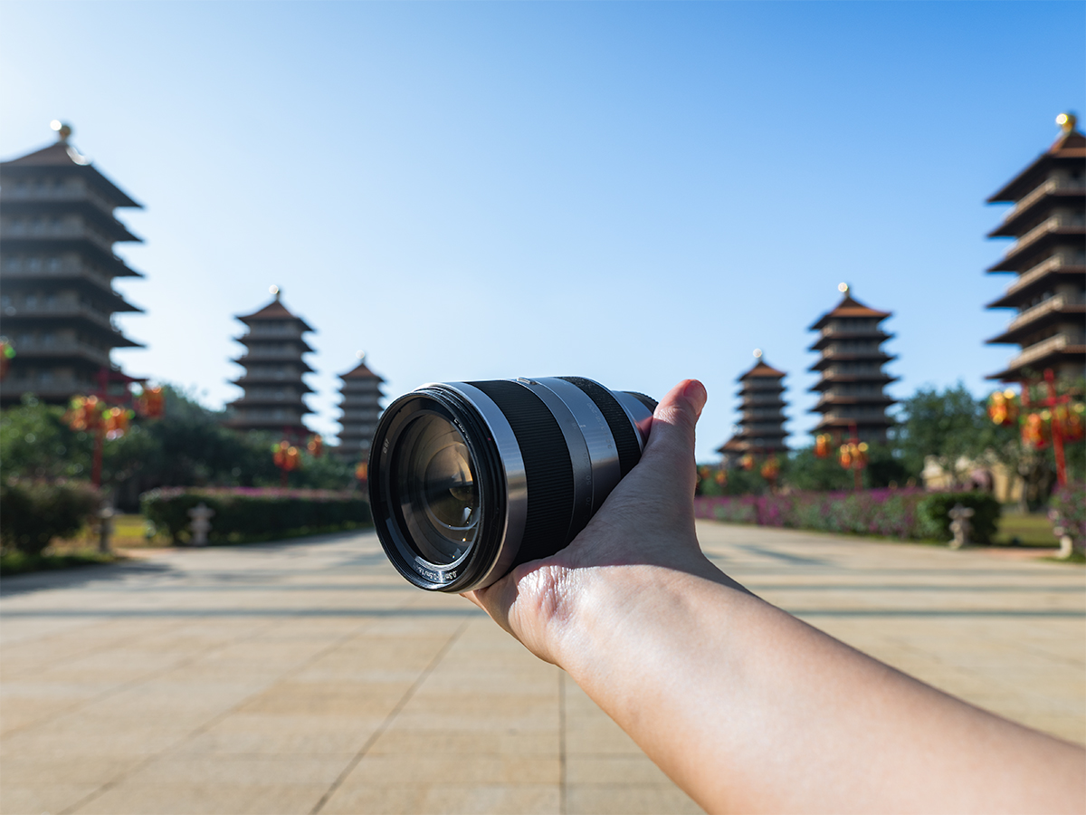 Holding a Sony 18-200mm f/3.5-6.3 which is the best affordable sony zoom lens for travel.