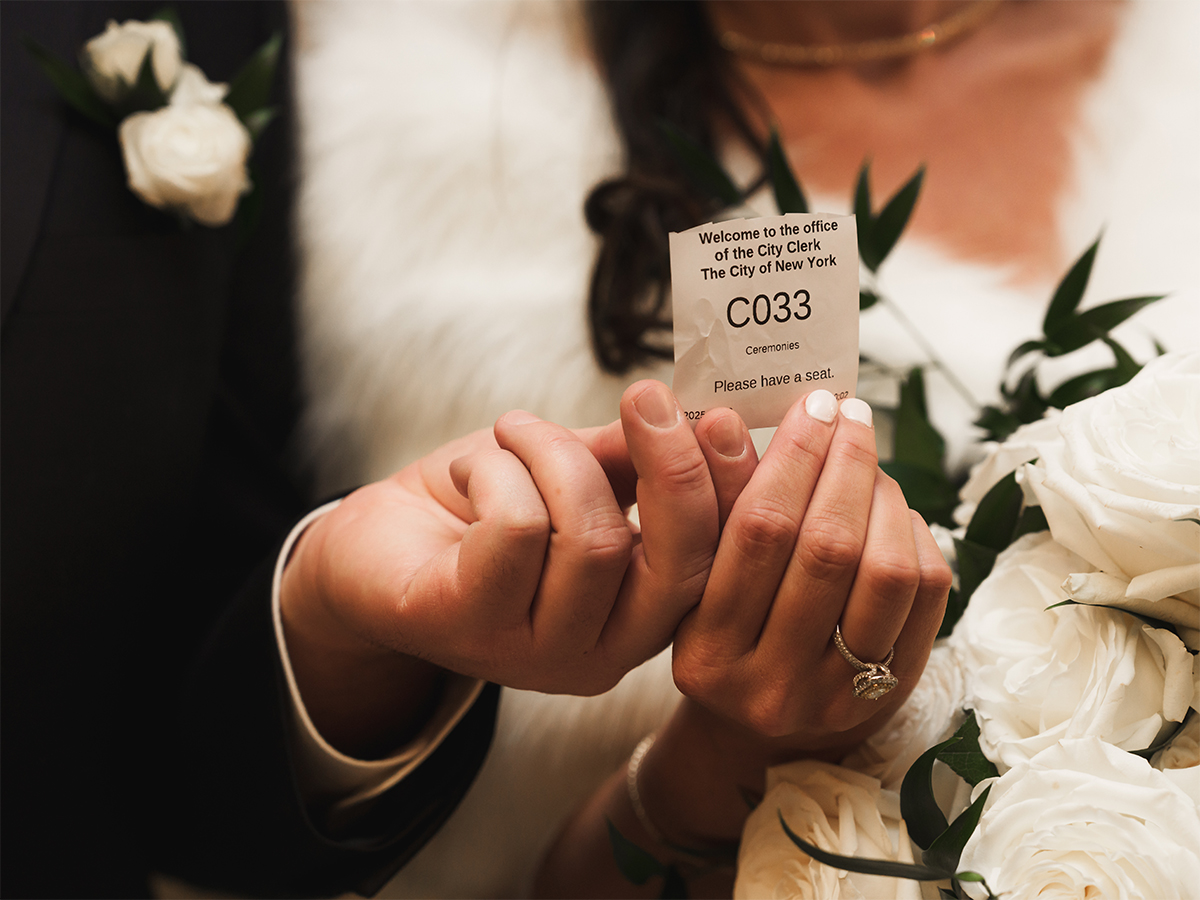 A couple doing their nyc city hall elopement holds their ceremony ticket.