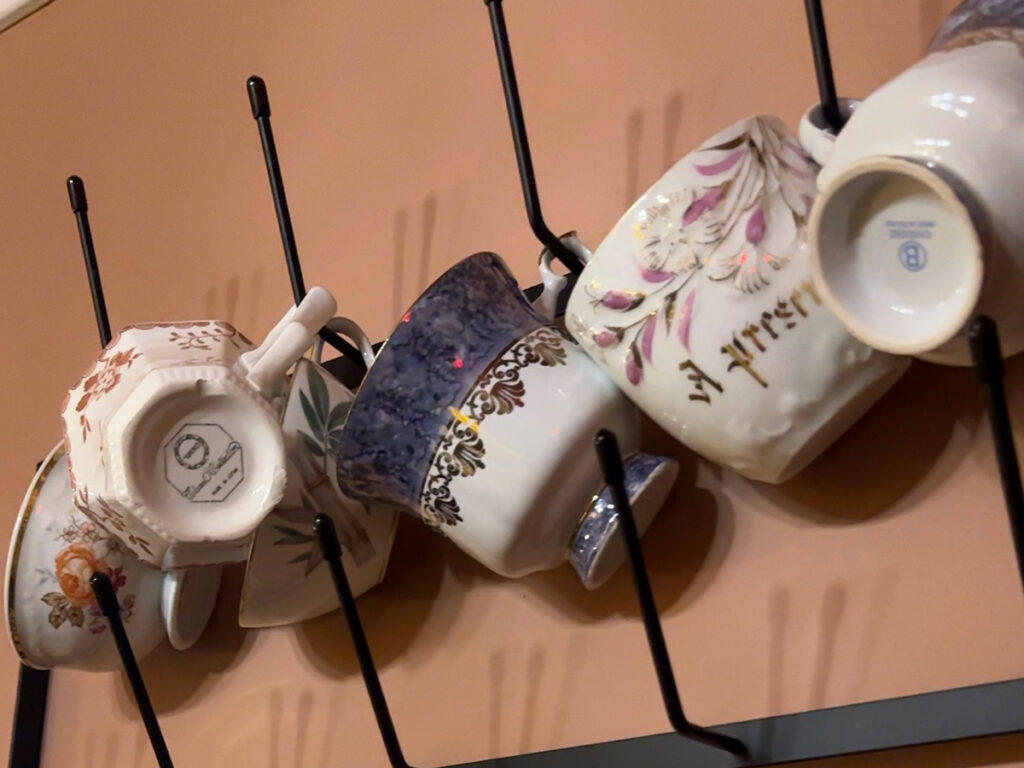 Mismatched vintage china teacups displayed on a wall rack at The Parlour, Brooklyn High Low's sister tea room in Park Slope