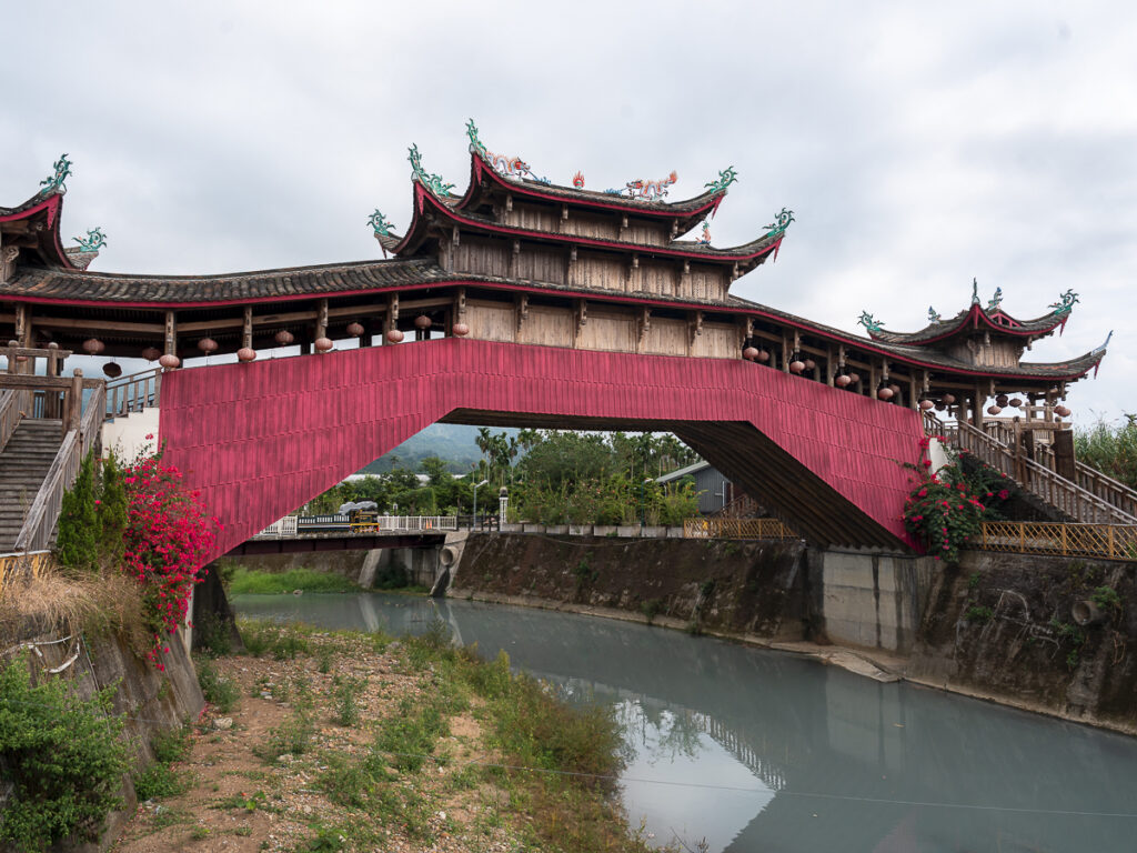 The red Taishun Gallery Bridge replica beside Wuchang Temple in Jiji Township, modeled after the wooden arch bridges of Taishun County, China.