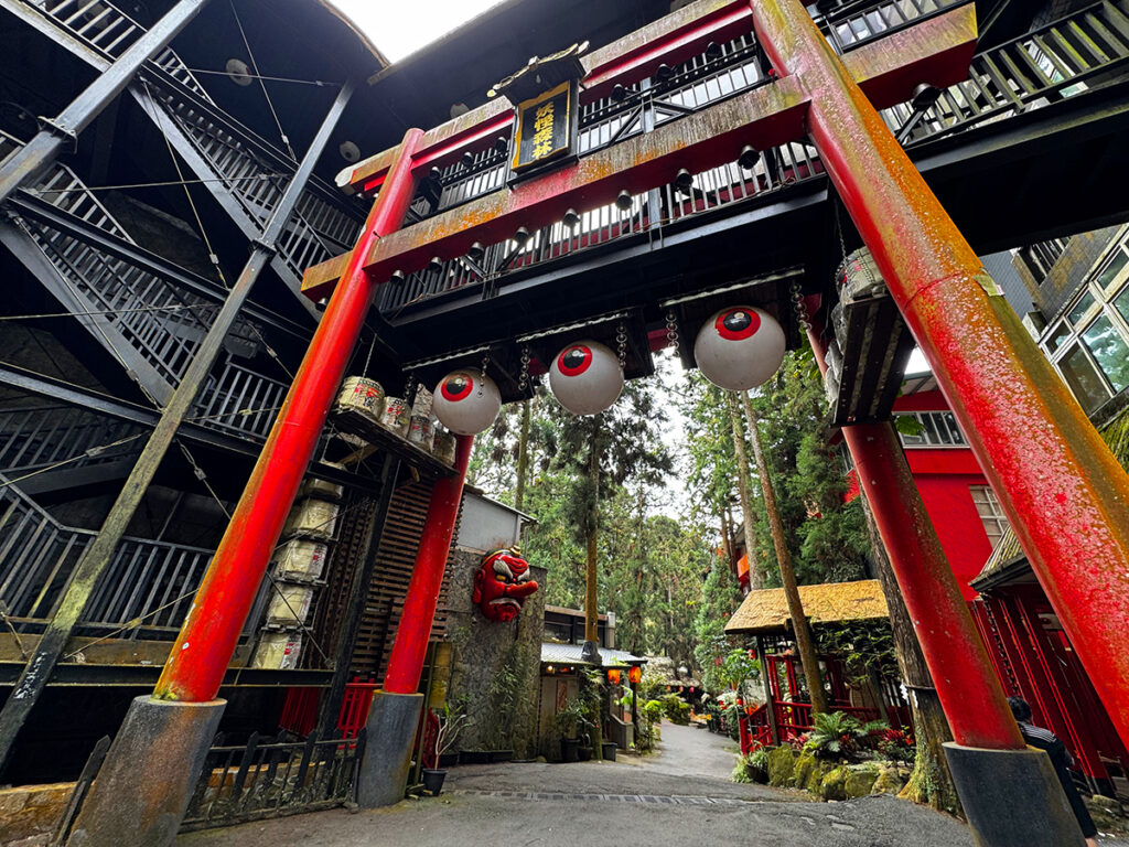 The red torii gate entrance to Xitou's Monster Village (ๅฆๆชๆ), decorated with giant eyeball lanterns and a monster mask.