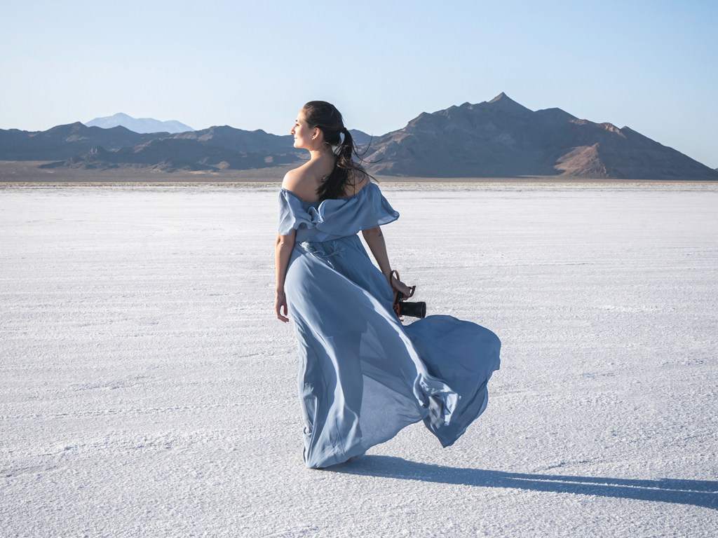 Erin Donahue is standing on the Bonneville Salt flats in a blue dress and holding her camera.