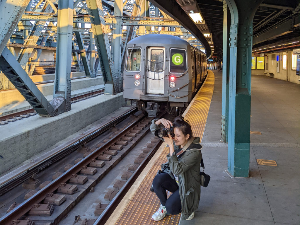 Erin Donahue taking a picture on a MTA subway platform with a G train behind her. 
