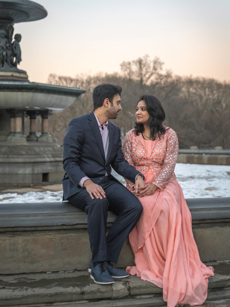 A couple looks at each other while sitting on the edge of the Bethesda fountain in Central Park.