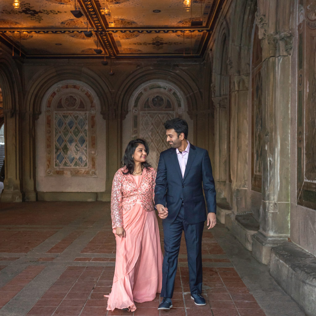 A happy couple holds hands and look at each other as they walk through the Bethesda Terrace in Central Park, NYC.