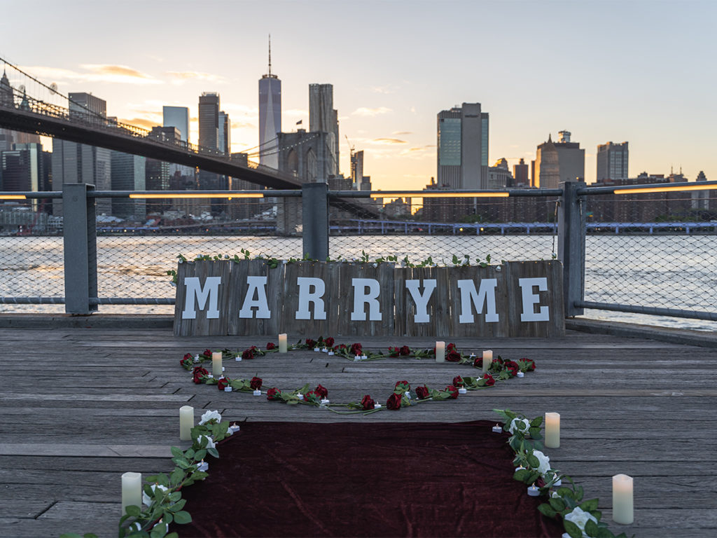 A "marry me" sign at Jane's Carousel in Brooklyn with the lower Manhattan skyline in the background.