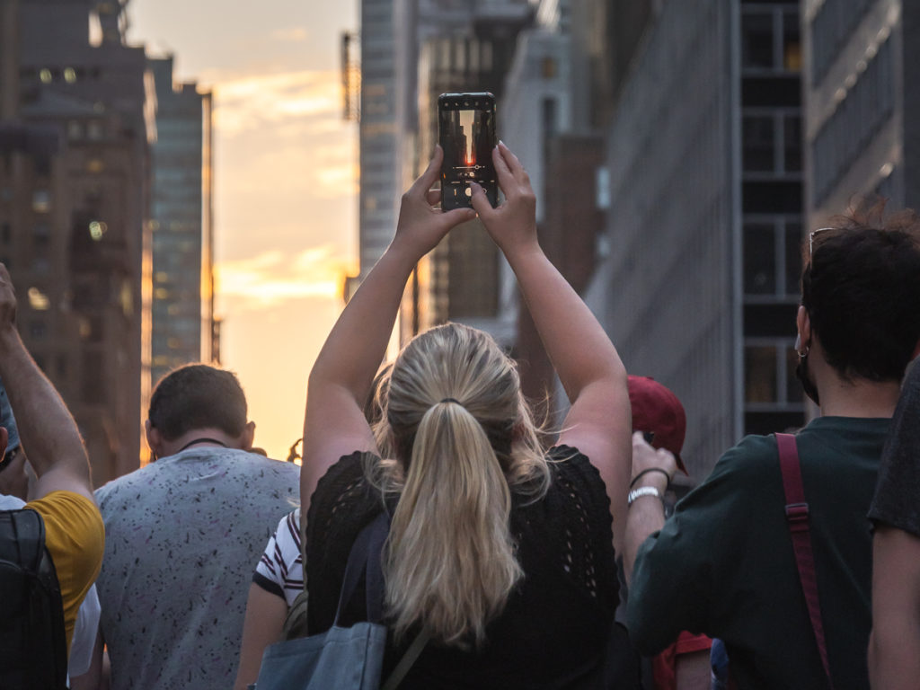 A passerby uses her phone for sun photography of Manhattanhenge.