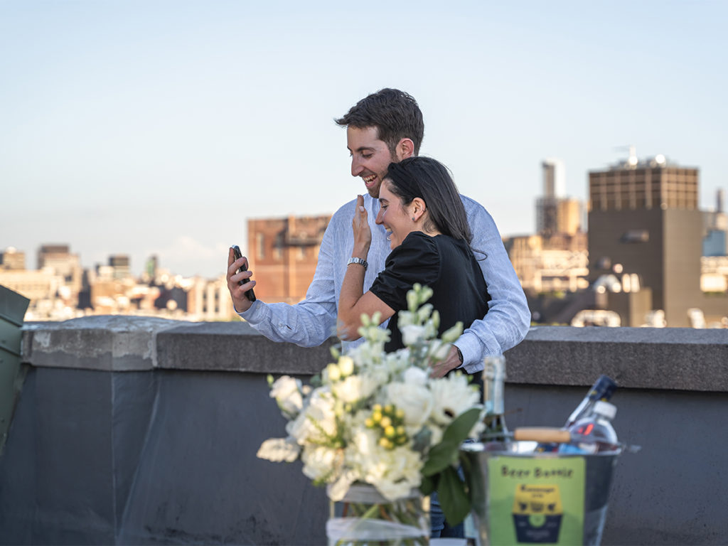 Candid moment between the couple calling their family after their West Village rooftop engagement. 