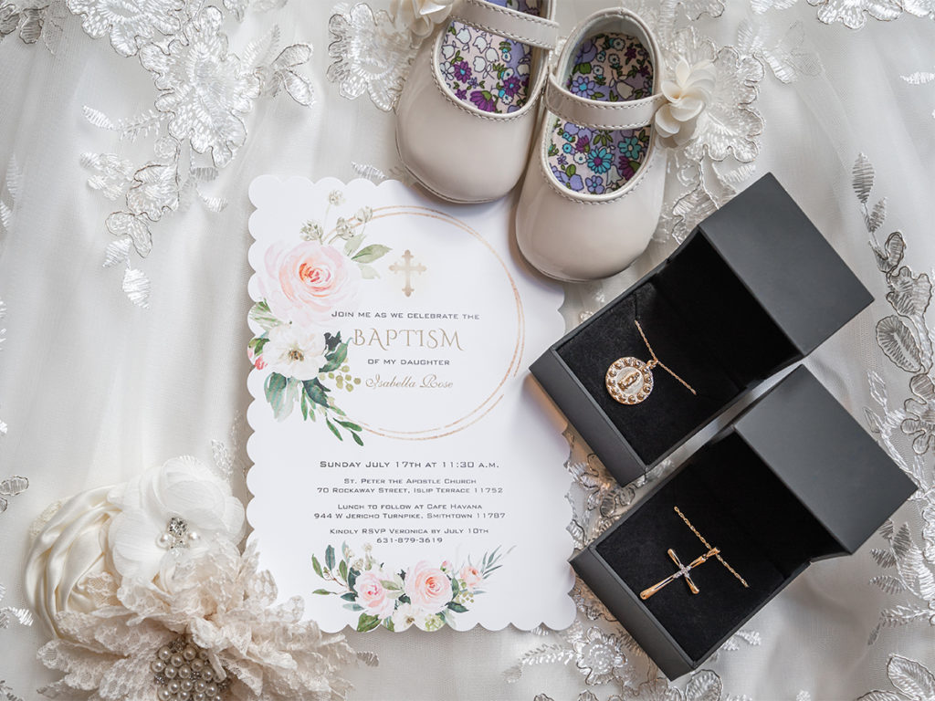 Invitation of a baby's baptism adorned with the baby's shoes and necklace in Long Island.