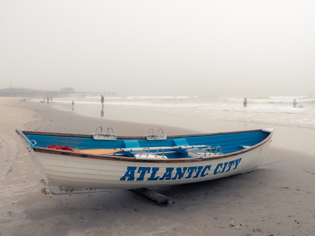 Row boat with "Atlantic City' sits on the sand of the beach.