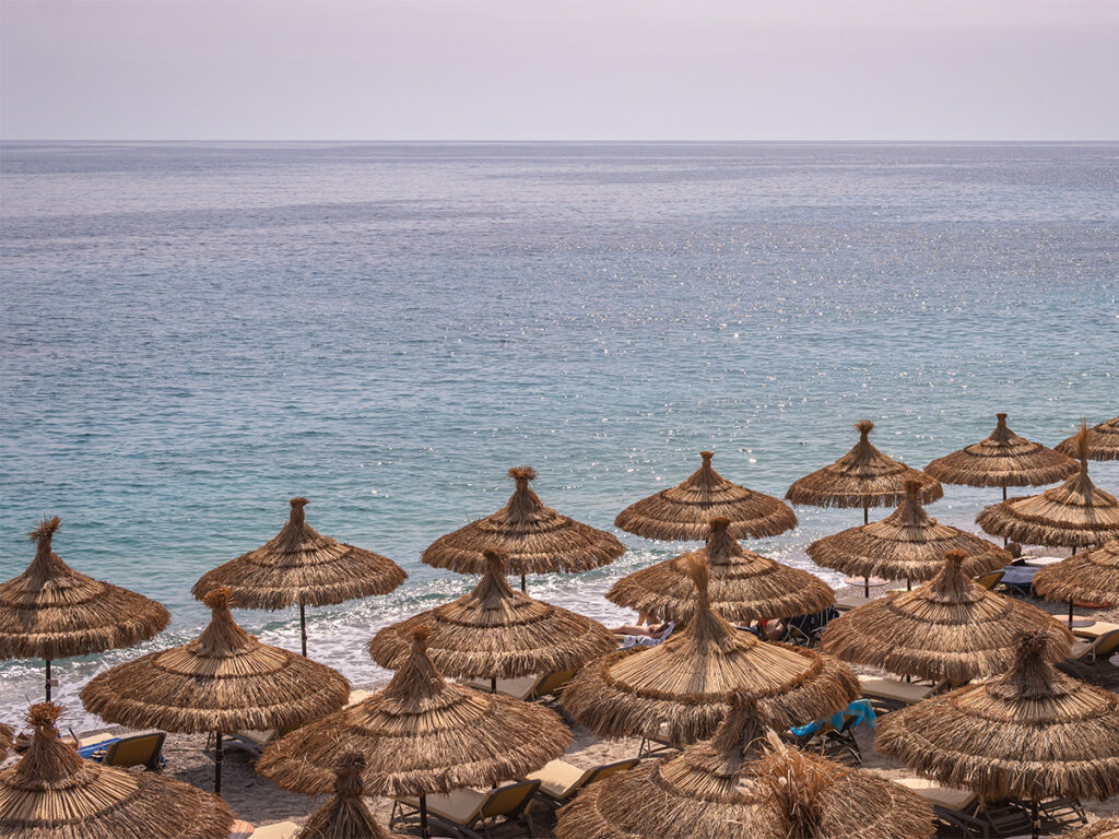 Rows of straw umbrellas line the beach town of Dhermi, Albania.