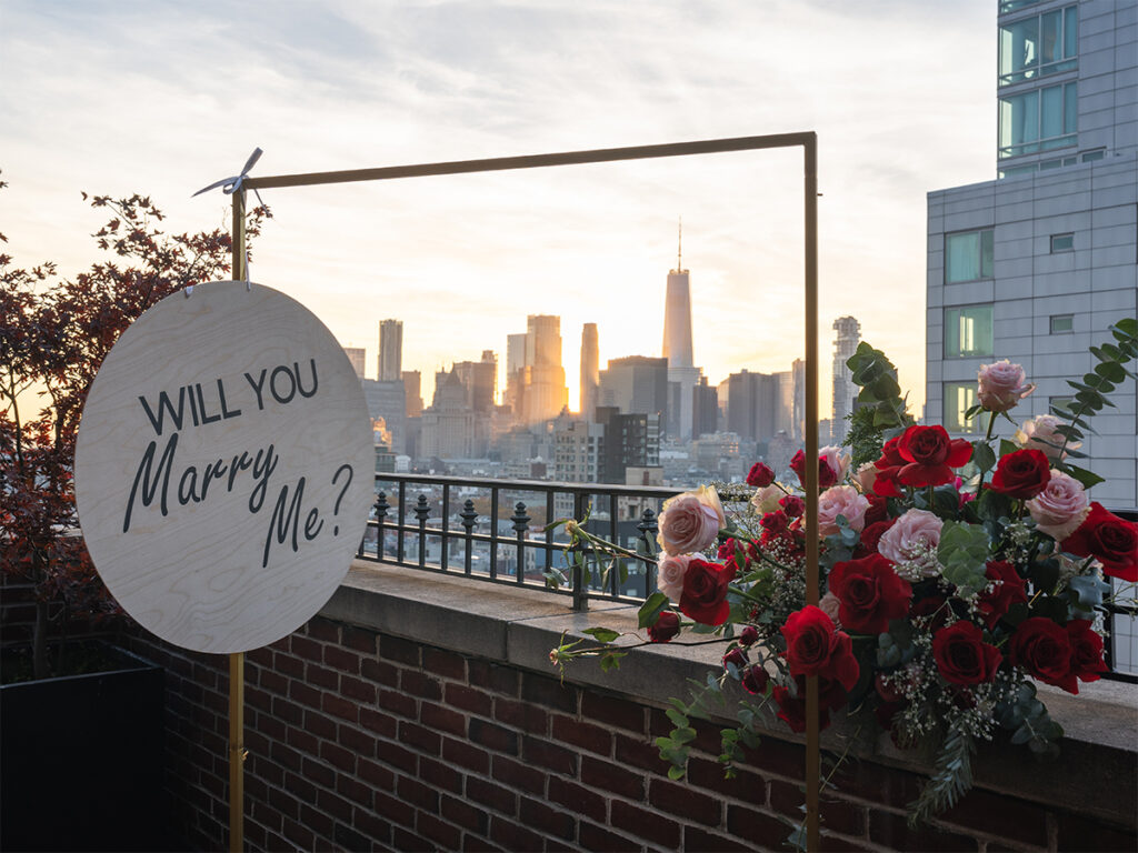 The Lower Manhattan skyline is framed with a "will you marry me" proposal set up on the terrace of The Ludlow Hotel.