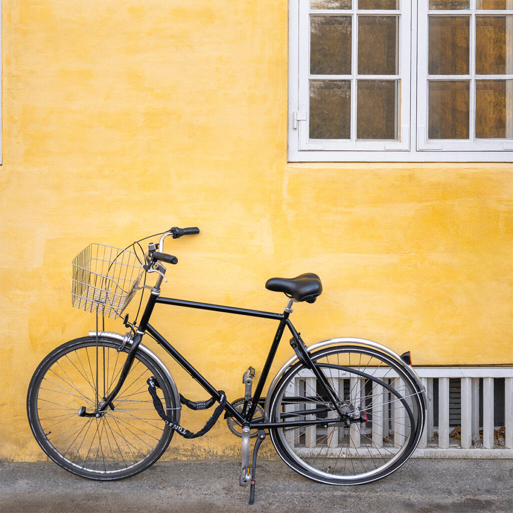 A bike stands in front of a yellow wall in Copenhagen. Biking is a great way to get around Copenhagen during a one week itinerary.
