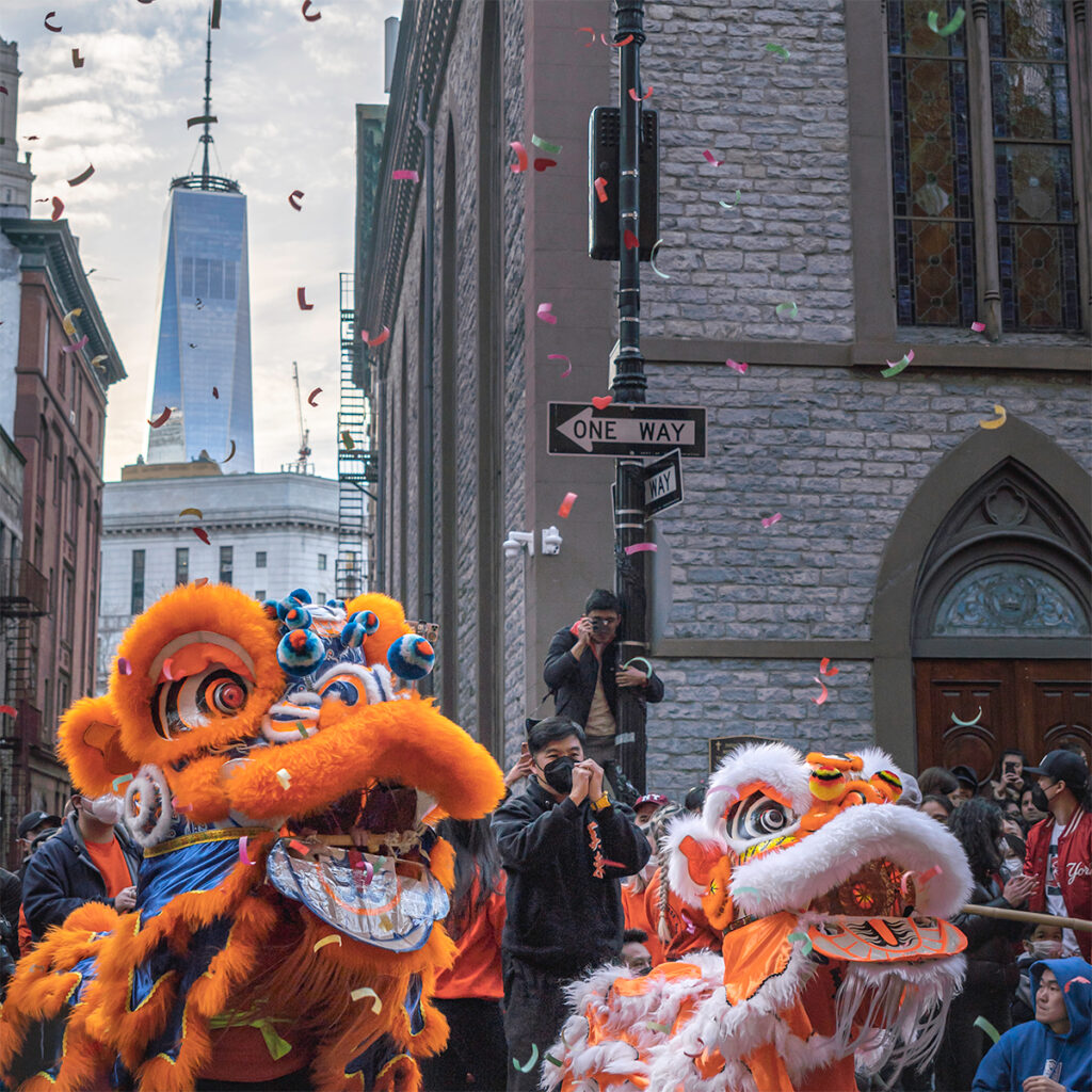 Photograph fireworks in NYC during Lunar New Year. Two lions dance in front of the World Trade Center in Chinatown.