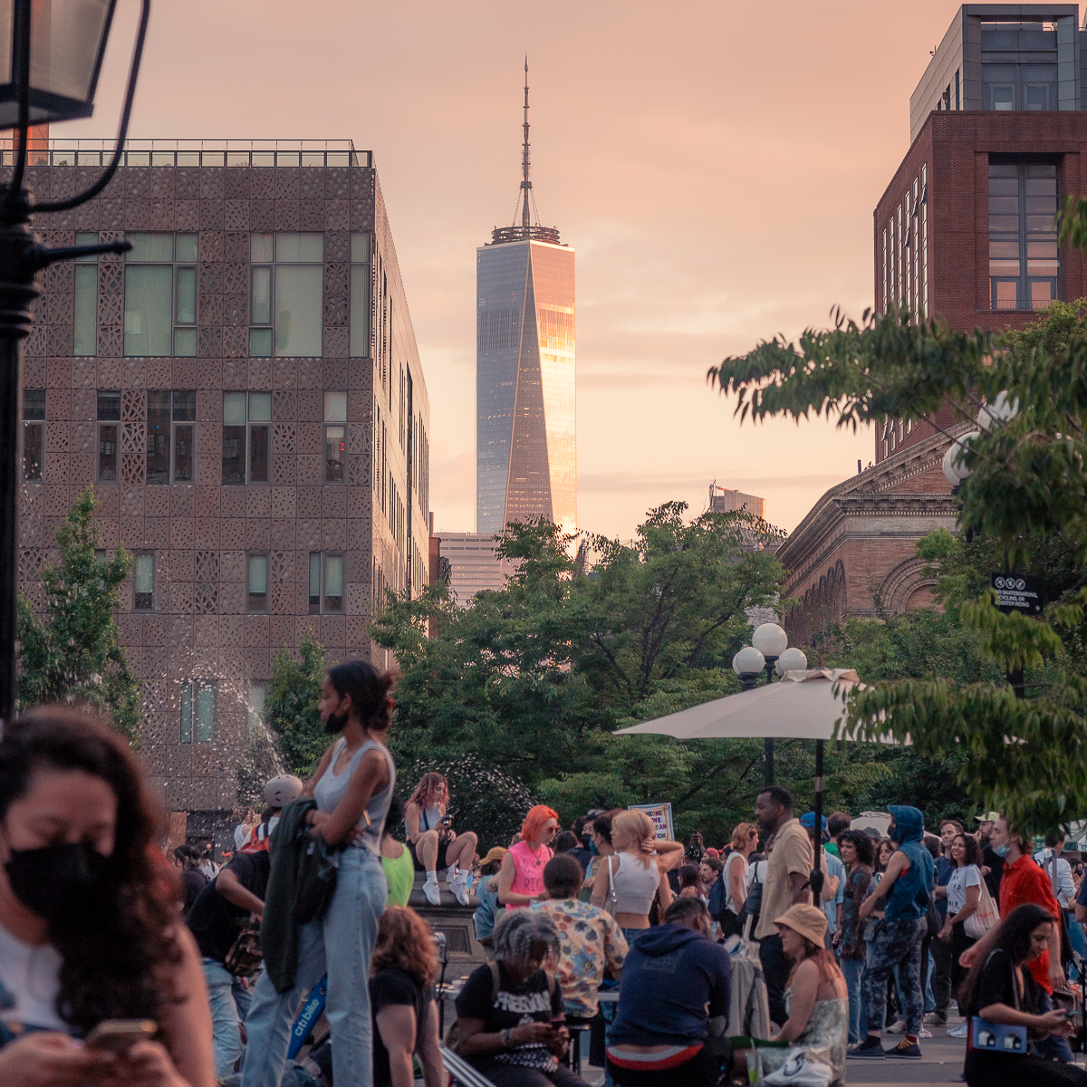 A group of people congregate at Washington Square Park during sunset with the Freedom Tower in the background.