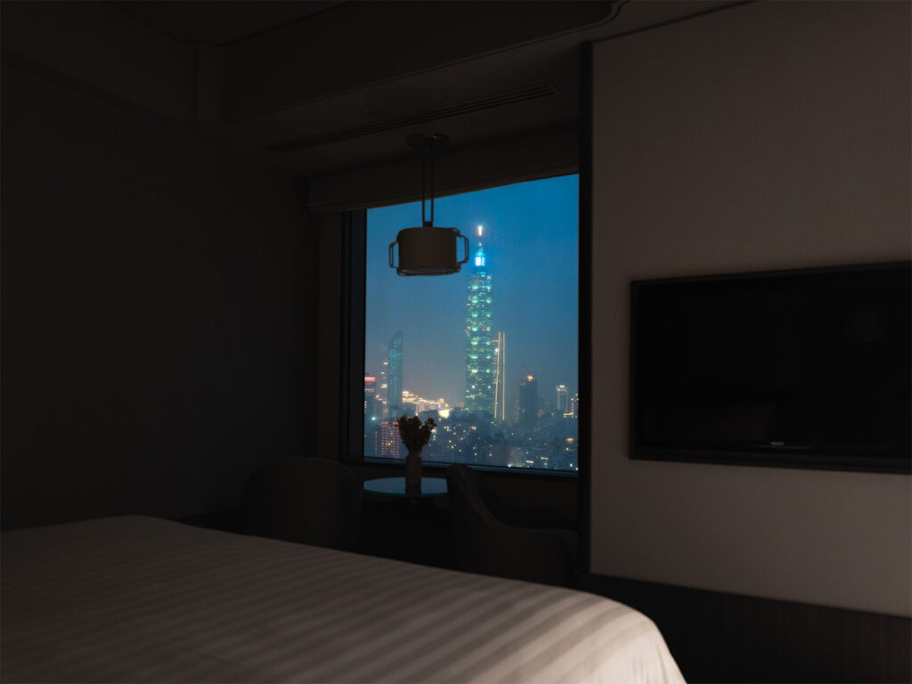 Night view of the Horizon Deluxe Room with the  the glittering Taipei 101 skyline outside the window.